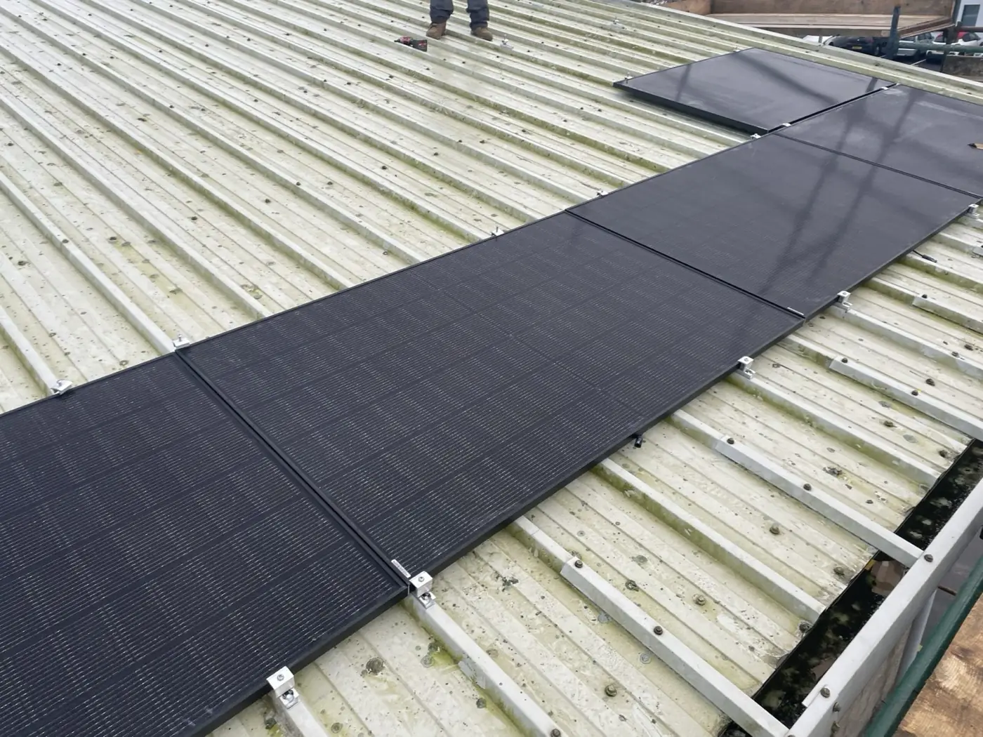 Black solar panels on mounting rails running across a corrugated commercial roof