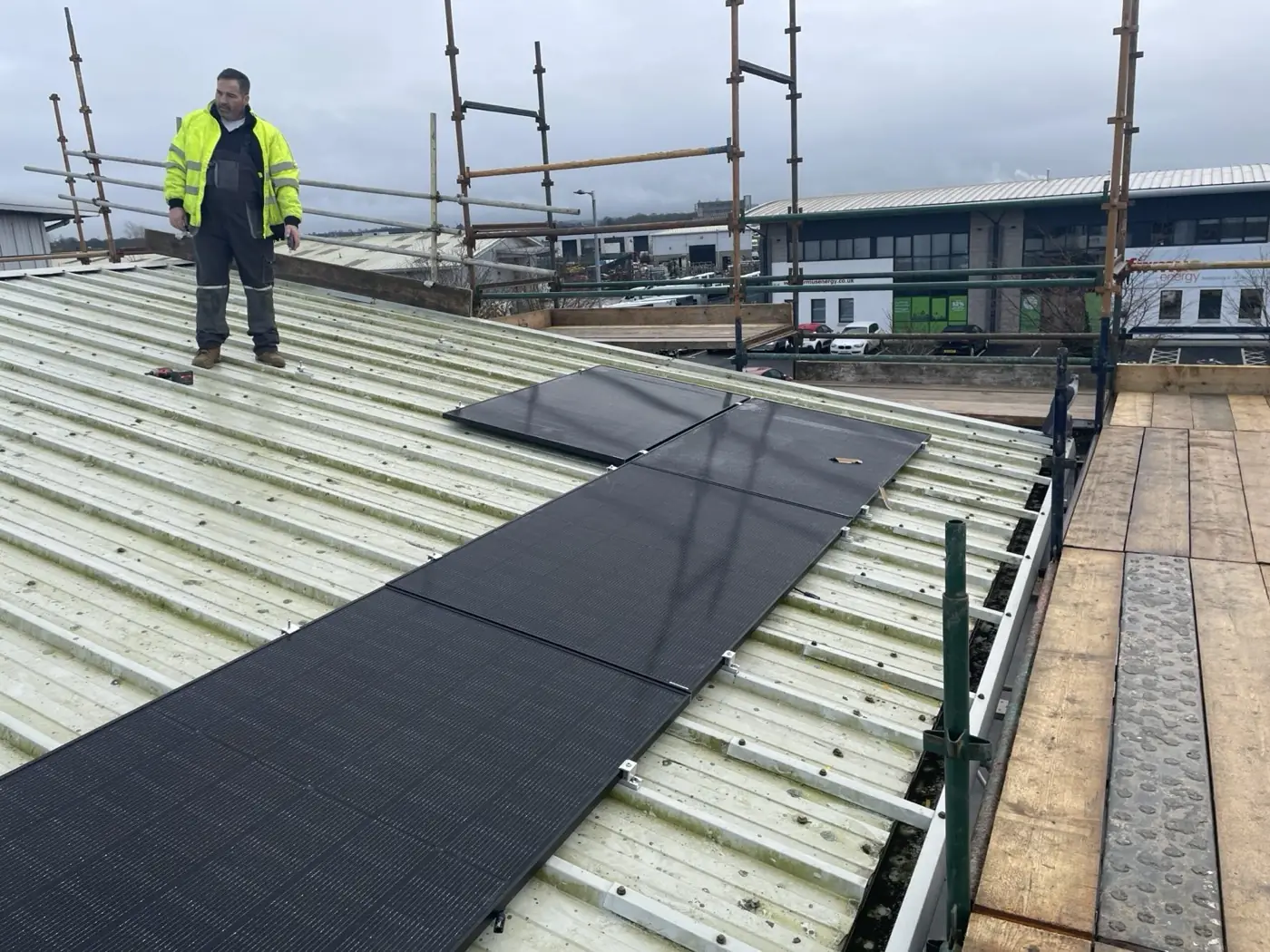 An installer in hi-vis standing on a commercial roof beside newly fitted solar panels