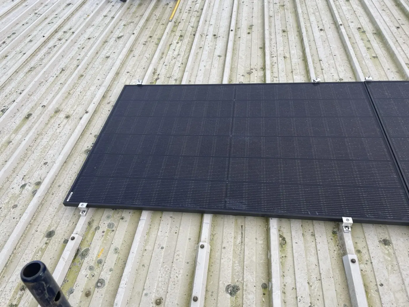 A black solar panel clamped to aluminium mounting rails on a corrugated metal roof