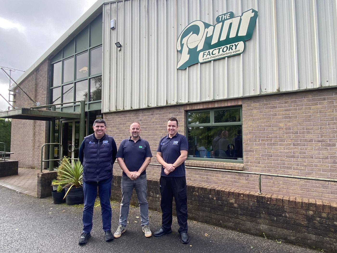 Three people standing in front of The Print Factory sign at handover of the solar installation