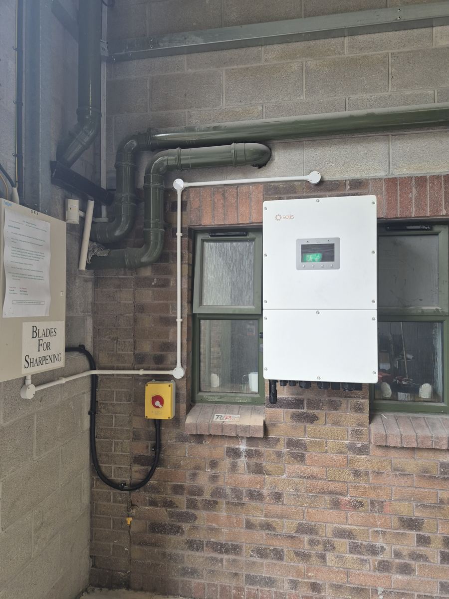Solis 40 kW three-phase inverter wall-mounted on a brick wall inside The Print Factory, with the emergency stop beside it