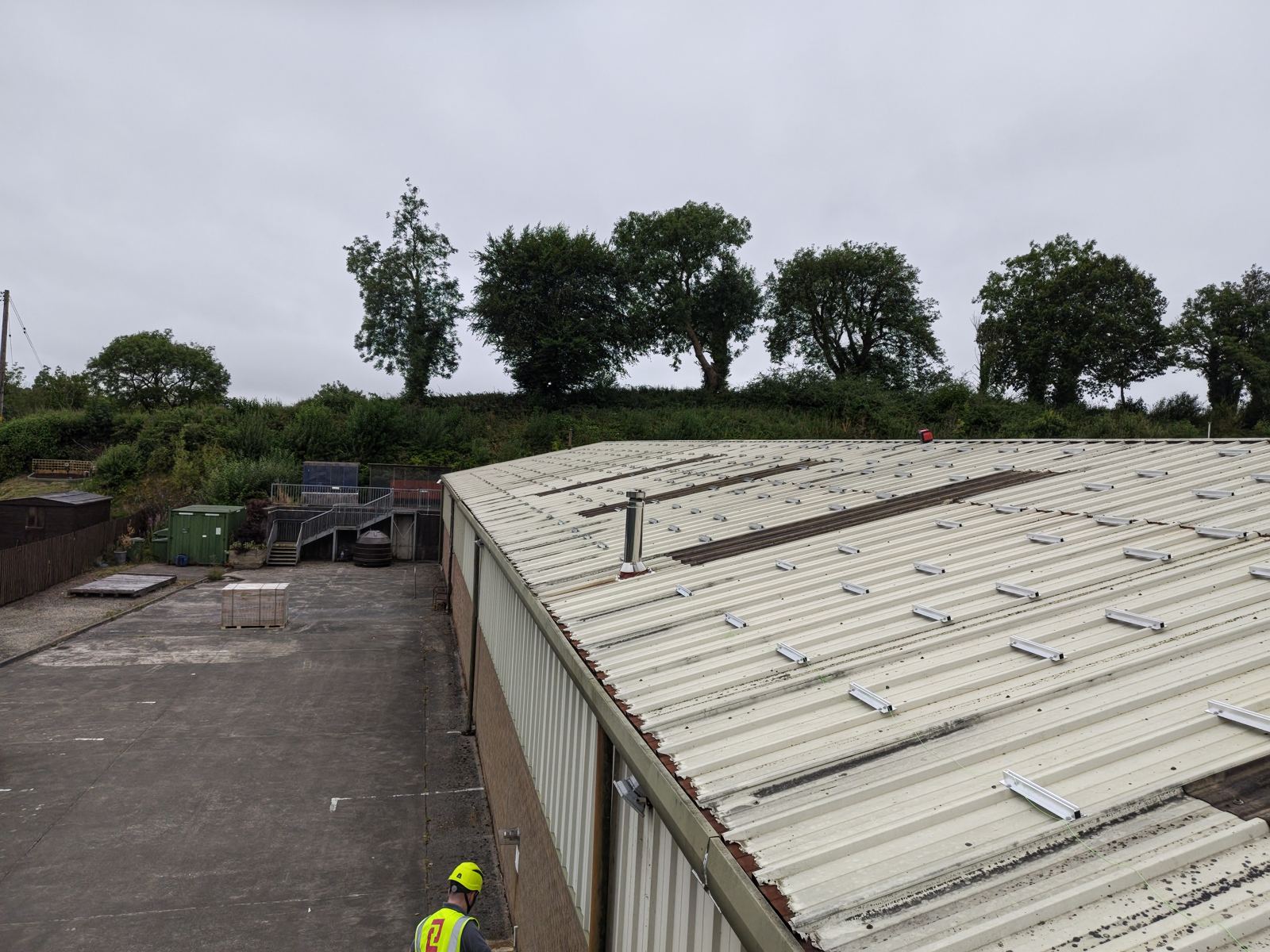 Mounting rails being set out across the bare steel roof of The Print Factory on install day, an installer in a hard hat in the foreground