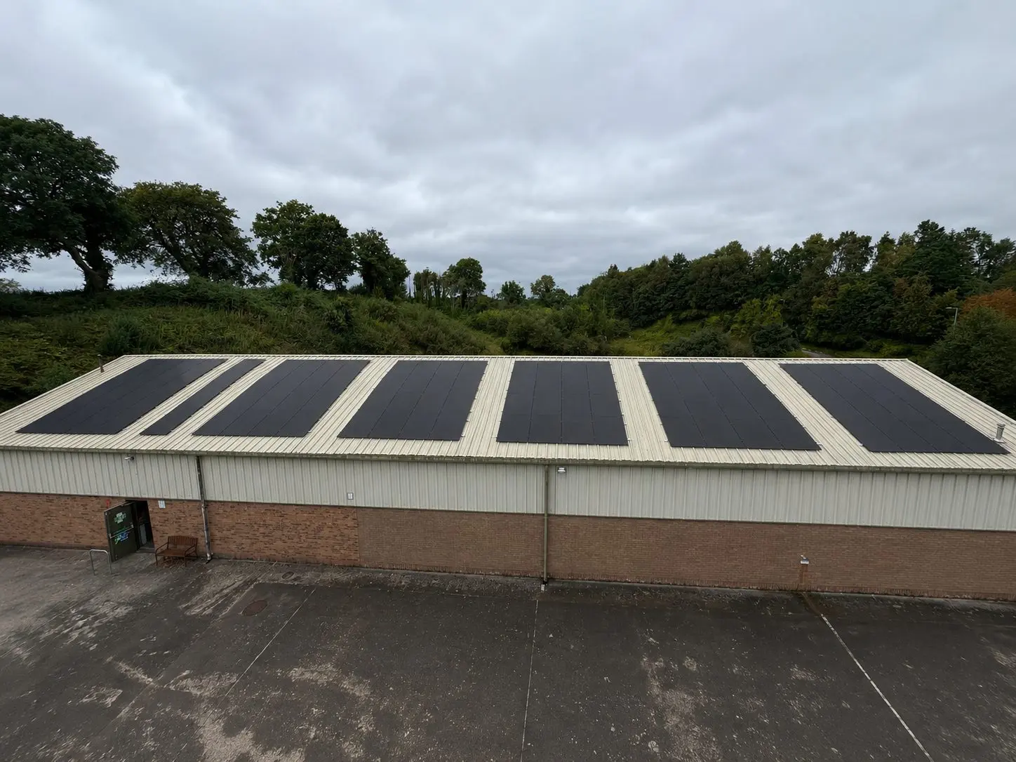 Rooftop solar array at The Print Factory, Enniskillen — six blocks of all-black panels on the pale steel roof of the production building, a B9 Renewables commercial install