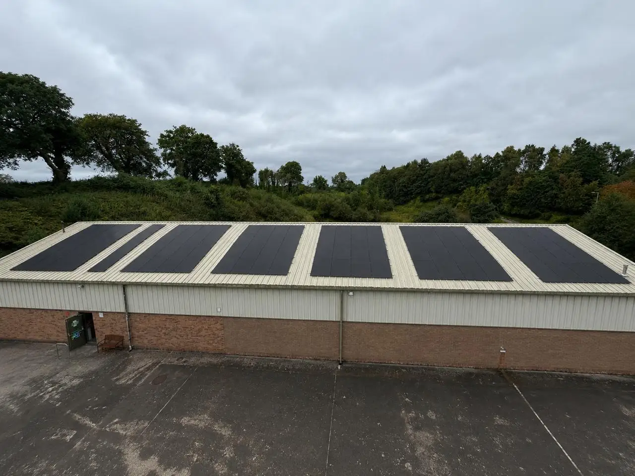 Six solar panels on the flat roof of a brick commercial building, with trees behind
