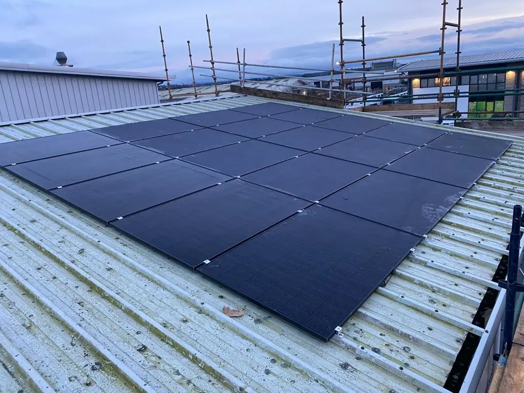 Black solar panels on a corrugated metal roof, with scaffolding behind