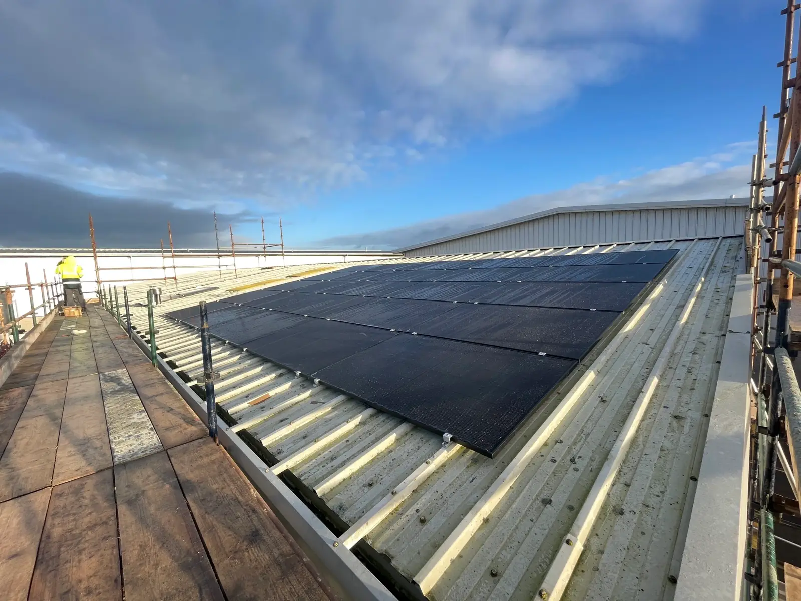Wide view along a scaffold walkway to a block of black solar panels on a metal roof
