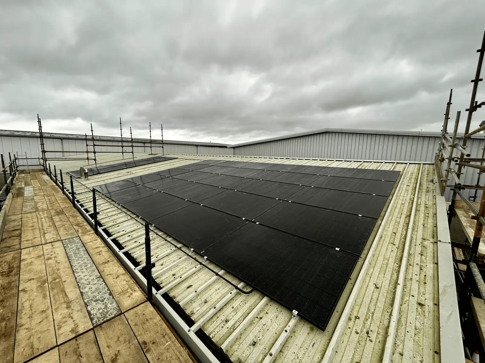 Black solar array on a metal roof under a grey sky, with scaffolding at the edges